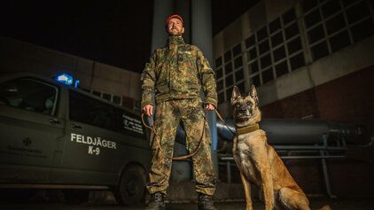 Ein Soldat der Feldjägertruppe steht mit seinem Diensthund vor einem Fahrzeug der Bundeswehr
