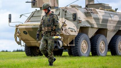 Ein Soldat der Bundeswehr geht vor einem Bundeswehrfahrzeug Fuchs entlang