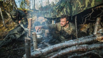 Ein Soldat der Bundeswehr kocht am Feuer seine Mahlzeit