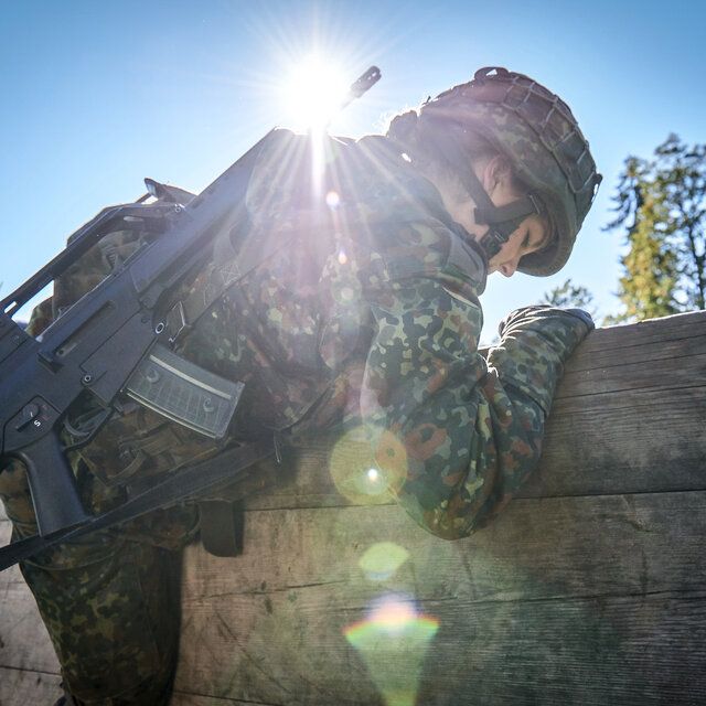 Eine Soldatin überwindet eine Hinderniswand mit ihrer Ausrüstung und dem Gewehr G36.