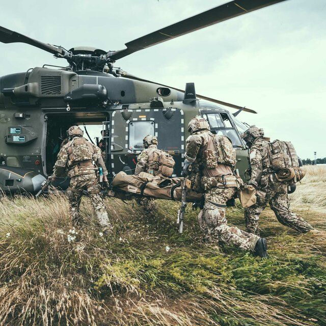 Soldaten bringen einen verwundeten Kameraden mit einer Trage zum Hubschrauber um diesen abtransportieren zu können.