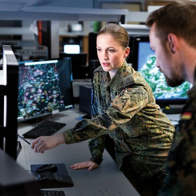 Eine Soldatin zeigt einem Soldaten etwas am Monitor in einer Kommandozentrale